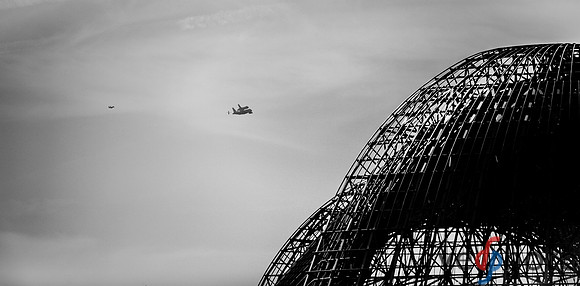 Space Shuttle Endeavour fades into the distance behind NASA Ames hangar